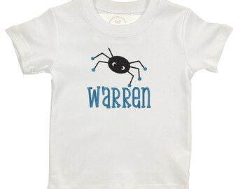 Puede incluir: Camiseta blanca de manga corta con una araña negra y ojos azules. El texto "Warren" está bordado en azul debajo de la araña.