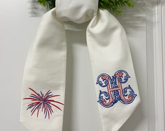 May include: White fabric bow with red, white, and blue embroidered fireworks and a blue and red embroidered letter H.