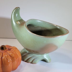 May include: A green ceramic cornucopia bowl with a brown base and a small orange ceramic pumpkin.