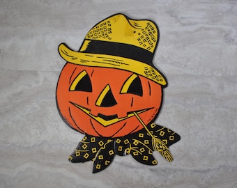 May include: A vintage Halloween decoration of a jack-o'-lantern wearing a straw hat with a black band and a black and yellow patterned scarf. The jack-o'-lantern has a wide smile and a straw sticking out of its mouth.