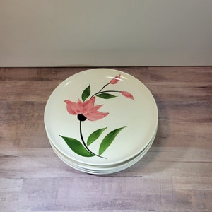 Könnte beinhalten: Ein Stapel von vier weißen Keramik-Dinnertellern mit einem Design aus einer rosa Blume und grünen Blättern.