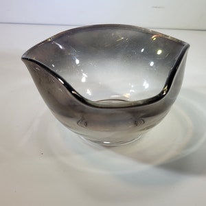 May include: A clear glass bowl with a wavy rim and a gradient of gray to clear. The bowl is sitting on a white surface.