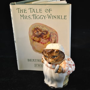 May include: A ceramic figurine of Mrs. Tiggy-Winkle from Beatrix Potter's book "The Tale of Mrs. Tiggy-Winkle". The figurine is brown and white with red and white checkered accents. The figurine is holding a small brush in her right hand.