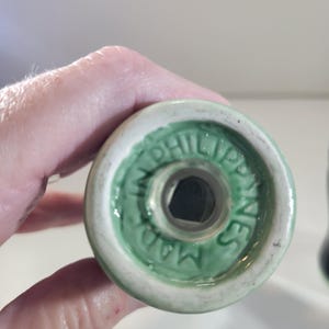 K&ouml;nnte beinhalten: Nahaufnahme des Bodens eines wei&szlig;en und gr&uuml;nen Keramik-Salzstreuers. Der Boden hat einen gr&uuml;nen Rand mit dem Text "MADE IN PHILIPPINES" in einem kreisf&ouml;rmigen Muster. Der Shaker hat eine sechseckige &Ouml;ffnung.