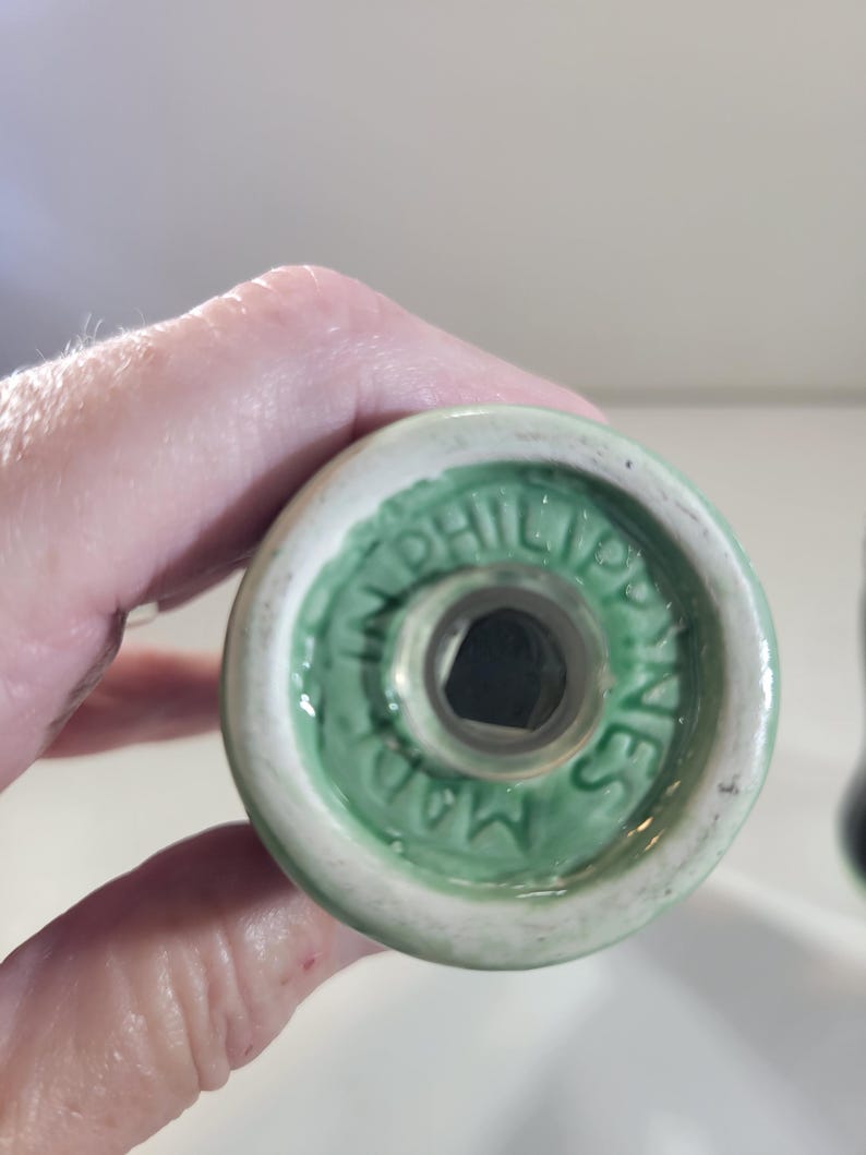 K&ouml;nnte beinhalten: Nahaufnahme des Bodens eines wei&szlig;en und gr&uuml;nen Keramik-Salzstreuers. Der Boden hat einen gr&uuml;nen Rand mit dem Text "MADE IN PHILIPPINES" in einem kreisf&ouml;rmigen Muster. Der Shaker hat eine sechseckige &Ouml;ffnung.