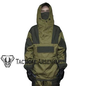Puede incluir: Anorak táctico verde oliva y negro con capucha y cubrecara. El anorak tiene un bolsillo frontal grande y parches en los hombros. El texto "Tactical Arsenal" es visible en la parte inferior izquierda.