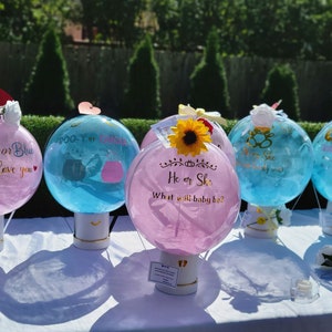 Puede incluir: Cinco globos de revelaci&oacute;n de g&eacute;nero en forma de globos aerost&aacute;ticos. Los globos est&aacute;n decorados con colores rosa y azul y tienen mensajes como "Rosa o Azul Te queremos", "Chico o Chica", "&Eacute;l o Ella &iquest;Qu&eacute; ser&aacute; el beb&eacute;?" y "Centellea Centellea Peque&ntilde;a Estrella".