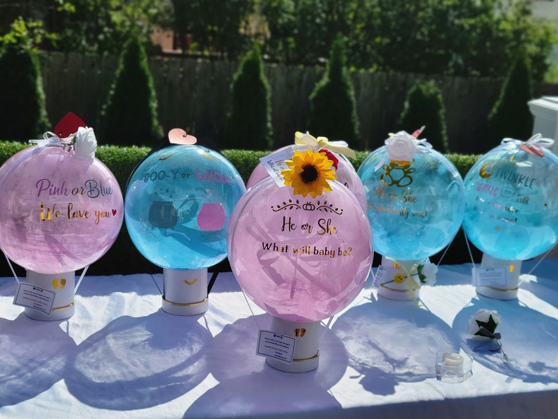 Puede incluir: Cinco globos de revelaci&oacute;n de g&eacute;nero en forma de globos aerost&aacute;ticos. Los globos est&aacute;n decorados con colores rosa y azul y tienen mensajes como "Rosa o Azul Te queremos", "Chico o Chica", "&Eacute;l o Ella &iquest;Qu&eacute; ser&aacute; el beb&eacute;?" y "Centellea Centellea Peque&ntilde;a Estrella".