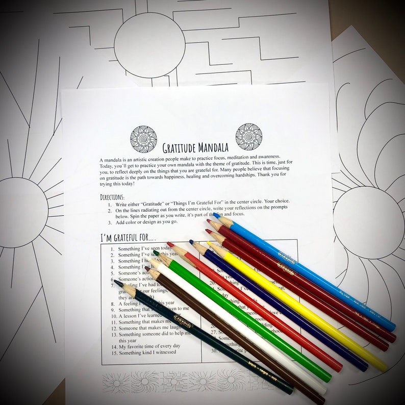 May include: A "Gratitude Mandala" coloring page with text and prompts, alongside a set of colored pencils. The page features a circular design with the words "Gratitude Mandala" at the top. The prompts encourage reflection on gratitude.