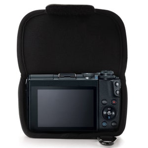 May include: A black camera with a large screen is inside a black padded case. The camera has a variety of buttons and controls, including a dial for ISO, a menu button, and a playback button.
