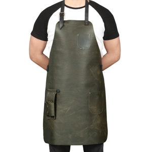 May include: A dark green leather apron with adjustable straps, a large pocket, and two smaller pockets. The apron has a distressed look and is made of high-quality leather.