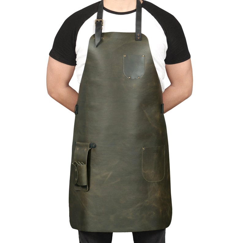 May include: A dark green leather apron with adjustable straps, a large pocket, and two smaller pockets. The apron has a distressed look and is made of high-quality leather.
