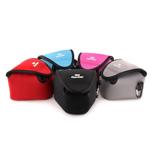 Op de afbeelding: Vijf cameralezenetuis in verschillende kleuren: rood, blauw, roze, zwart en grijs. Elk etui heeft een ritssluiting en een kleine lus om een ​​bandje aan te bevestigen. De etuis zijn gemaakt van een zacht, flexibel materiaal en hebben de tekst "HCS MageGear" erop gedrukt.