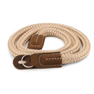 May include: A beige camera strap made of braided rope with brown leather accents and a silver metal ring.