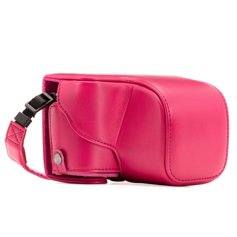 Pu&ograve; includere: Una custodia per fotocamera in pelle rosa con una tracolla nera regolabile. La custodia ha una patta che si chiude con un bottone a pressione.