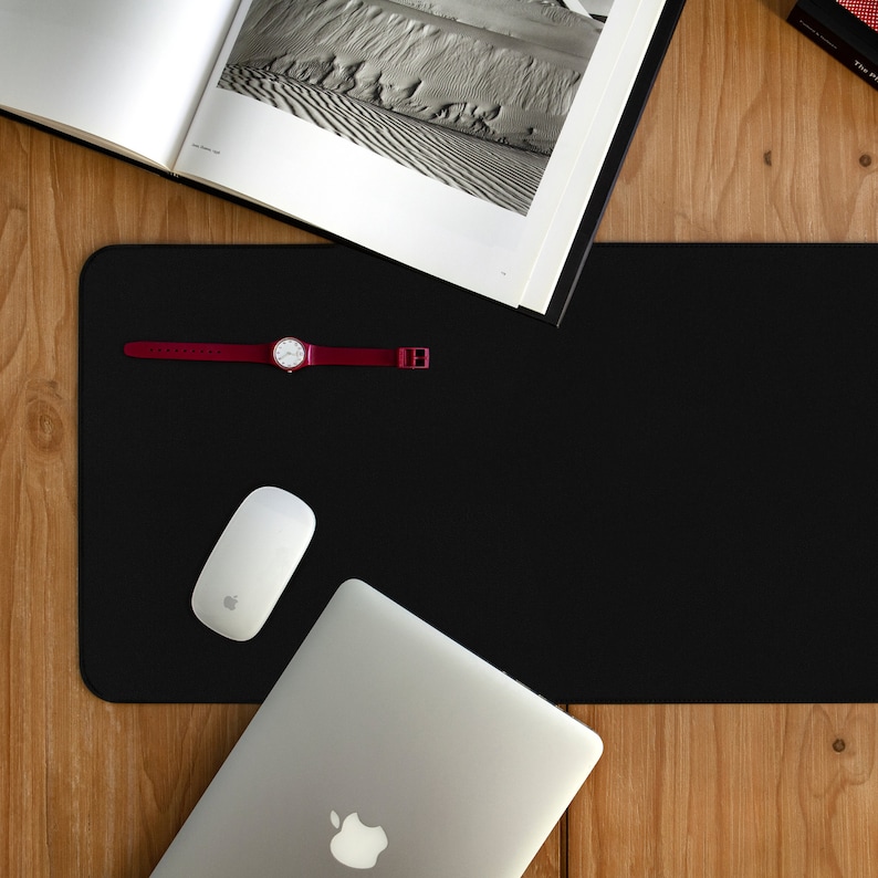 May include: A black desk mat with a red wristwatch, a white computer mouse, and a silver laptop computer.