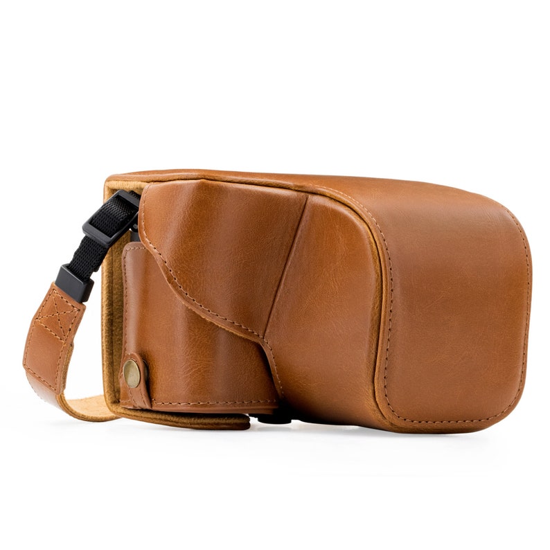 Pu&ograve; includere: Una custodia per fotocamera in pelle marrone con una tracolla. La custodia ha una patta che copre l'obiettivo della fotocamera.