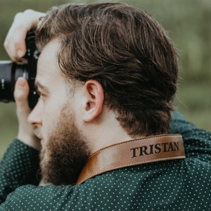 May include: A brown leather camera strap with the name "Tristan" embossed in white lettering.