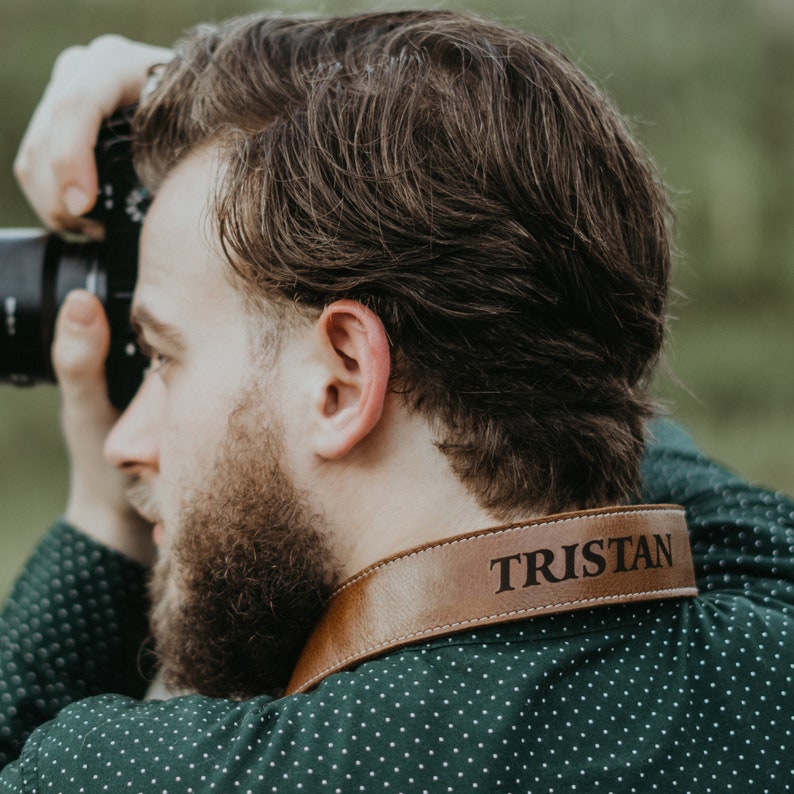 May include: A brown leather camera strap with the name "Tristan" embossed in white lettering.
