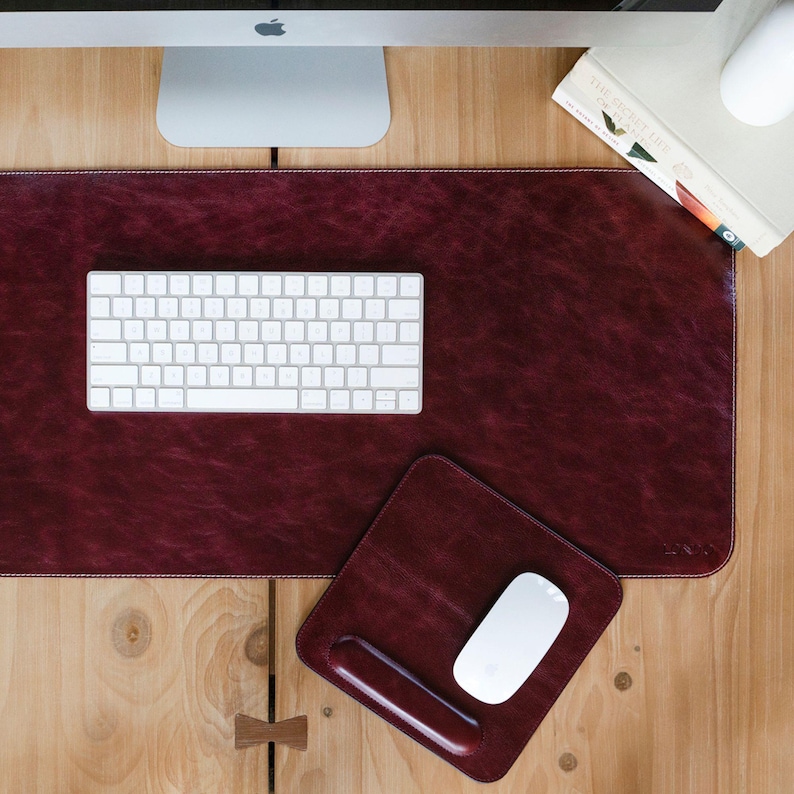 May include: A burgundy leather desk mat with a white keyboard and mouse. The mat has a stitched edge and a small leather mouse pad with a pen holder.