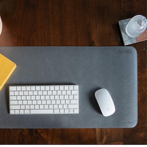 May include: A gray leather desk mat with the word "MARK" and "LONDO" printed on it. A white keyboard and a white mouse are on the mat.