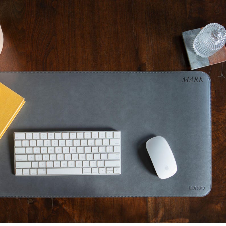 May include: A gray leather desk mat with the word "MARK" and "LONDO" printed on it. A white keyboard and a white mouse are on the mat.