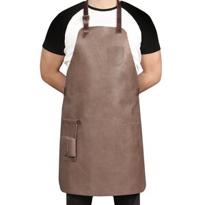 May include: A brown leather apron with adjustable straps, a large pocket on the front, and two smaller pockets on the sides.