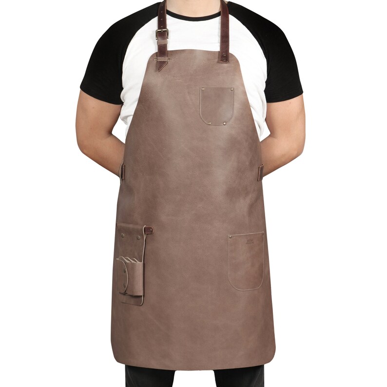 May include: A brown leather apron with adjustable straps, a large pocket on the front, and two smaller pockets on the sides.