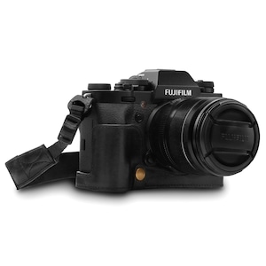 Könnte beinhalten: Eine schwarze Kamera mit einer schwarzen Ledertasche und einer schwarzen Objektivabdeckung. Die Kamera hat einen Riemen. Die Kameramarke ist FUJIFILM.