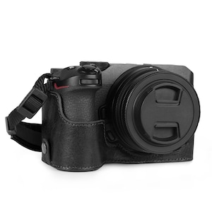 May include: Black leather camera case with a strap. The case is designed to fit a mirrorless camera with a lens attached.