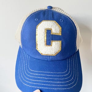 May include: A blue and white trucker hat with a gold and white letter "C" on the front.
