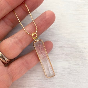 May include: A gold chain necklace with a clear quartz pendant. The pendant is a rectangular shape with a gold frame.