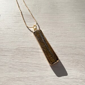 May include: A gold chain necklace with a long, rectangular pendant made of brown and gold stone.