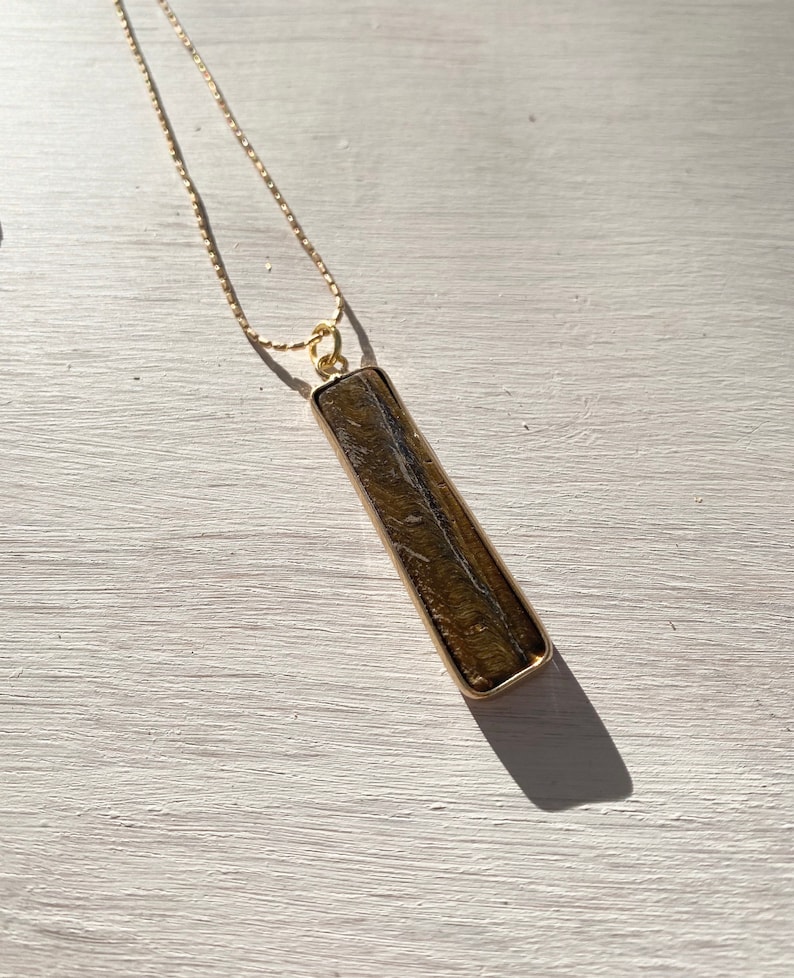 May include: A gold chain necklace with a long, rectangular pendant made of brown and gold stone.