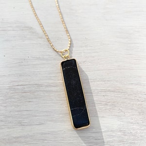May include: A gold chain necklace with a black rectangular pendant. The pendant has a marbled pattern and is set in a gold frame.