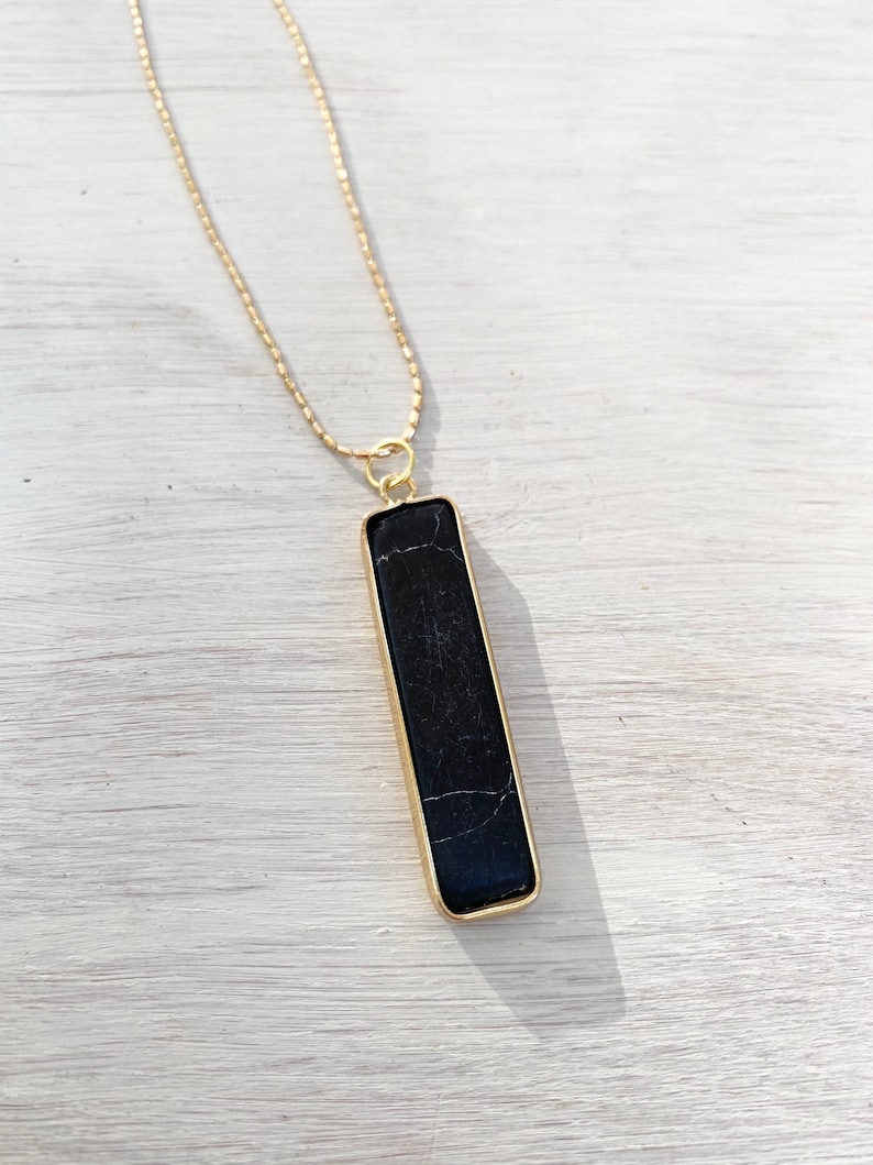 May include: A gold chain necklace with a black rectangular pendant. The pendant has a marbled pattern and is set in a gold frame.