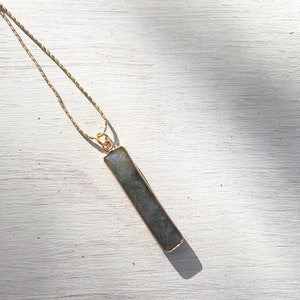 May include: A gold chain necklace with a long, rectangular, dark grey labradorite pendant.