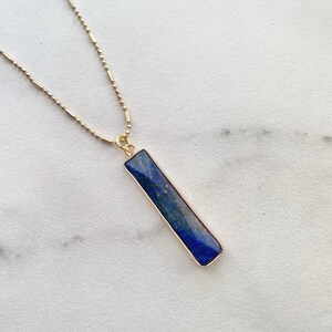 May include: A gold chain necklace with a rectangular lapis lazuli pendant. The pendant is a deep blue color with gold trim.