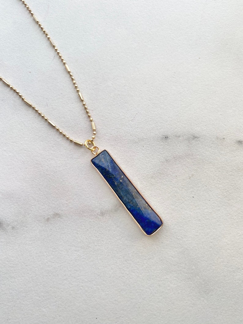 May include: A gold chain necklace with a rectangular lapis lazuli pendant. The pendant is a deep blue color with gold trim.
