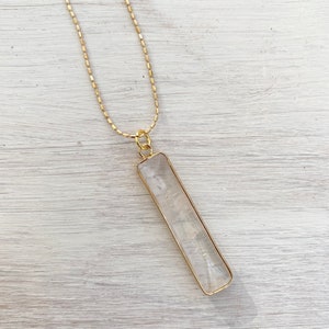 May include: A gold chain necklace with a clear rectangular pendant.
