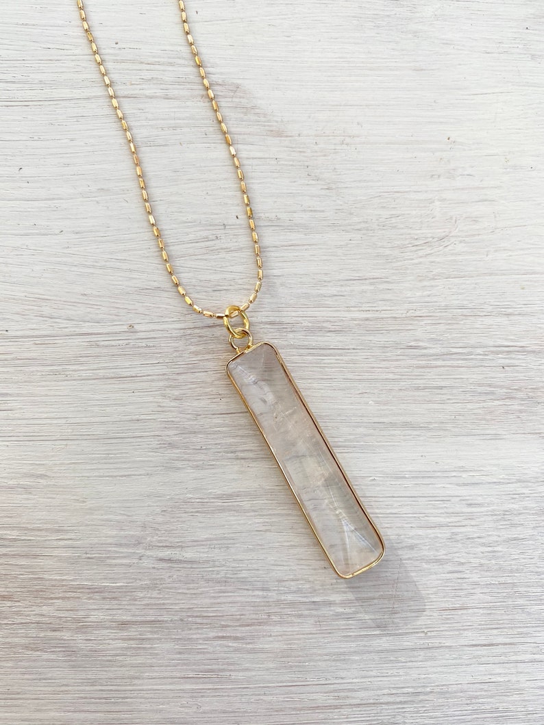 May include: A gold chain necklace with a clear rectangular pendant.