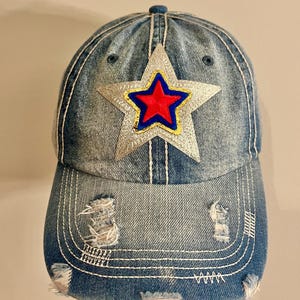May include: A blue denim baseball cap with a silver star patch featuring a red and blue star inside. The cap has distressed detailing and a curved brim.