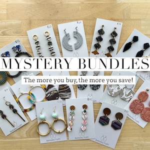 May include: A variety of handmade earrings displayed on cards with prices. The earrings are made from different materials, including wood, metal, beads, and fabric. The text "MYSTERY BUNDLES" and "The more you buy, the more you save!" is visible on the cards.