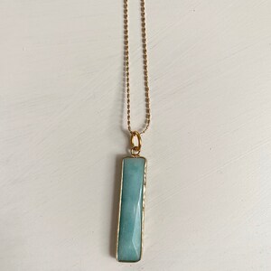 May include: A gold chain necklace with a light blue rectangular pendant. The pendant is made of a smooth, polished stone.