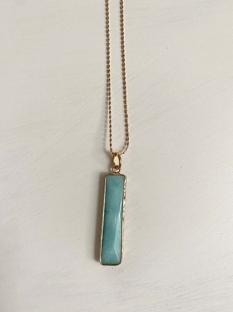 May include: A gold chain necklace with a light blue rectangular pendant. The pendant is made of a smooth, polished stone.
