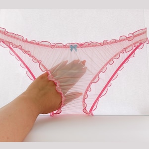 Könnte beinhalten: Rosa durchsichtige Dessous mit Rüschenbesatz und einer kleinen blauen Schleife.