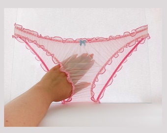 Pode incluir: Lingerie rosa transparente com renda, acabamento de babados e um pequeno laço azul.