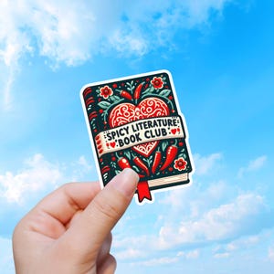 Könnte beinhalten: Ein Aufkleber mit einem Buchdesign, das ein Herz- und Chili-Pfeffer-Motiv zeigt. Das Buch ist schwarz mit roten Akzenten und dem Text "SPICY LITERATURE BOOK CLUB" auf einem Banner. Der Hintergrund ist ein hellblauer Himmel.