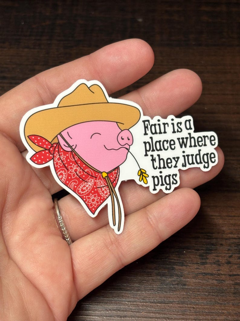 May include: A sticker depicting a cartoon pig in a cowboy hat and red bandana. The pig holds a piece of straw. The text on the sticker says "Fair is a place where they judge pigs."