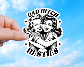 May include: A die-cut vinyl sticker featuring a black and white illustration of two women with vintage hairstyles hugging each other. The text BAD BITCH BESTIES is printed in a bold black font above and below the figures, accented by four stars.